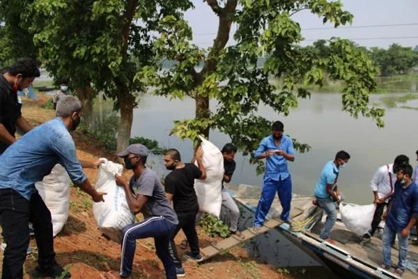Field teams and volunteers offloading grain sacks and emergency food rations from boats along inundated embankments.